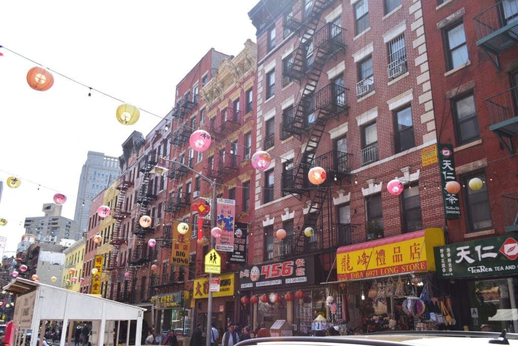 Colourful lanterns hang above a busy street lined with shops and red brick buildings in one of New York's vibrant neighbourhoods, Chinatown.