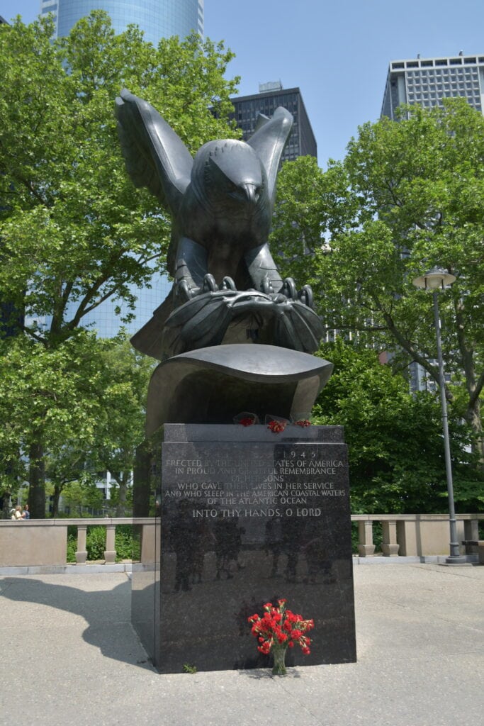 Large bronze eagle monument with flowers at its base, surrounded by trees and tall buildings—an iconic sight found in many parks in New York.