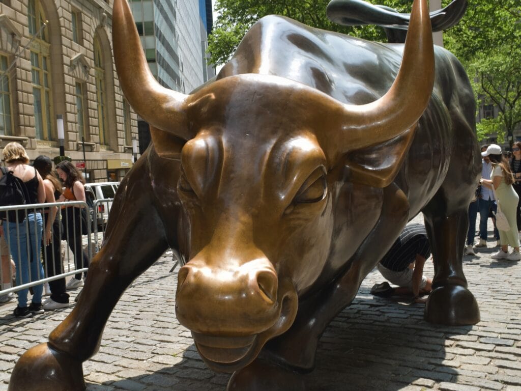 Close-up of the Charging Bull statue on a cobbled street in one of the vibrant neighbourhoods in New York, with people standing and looking around it.