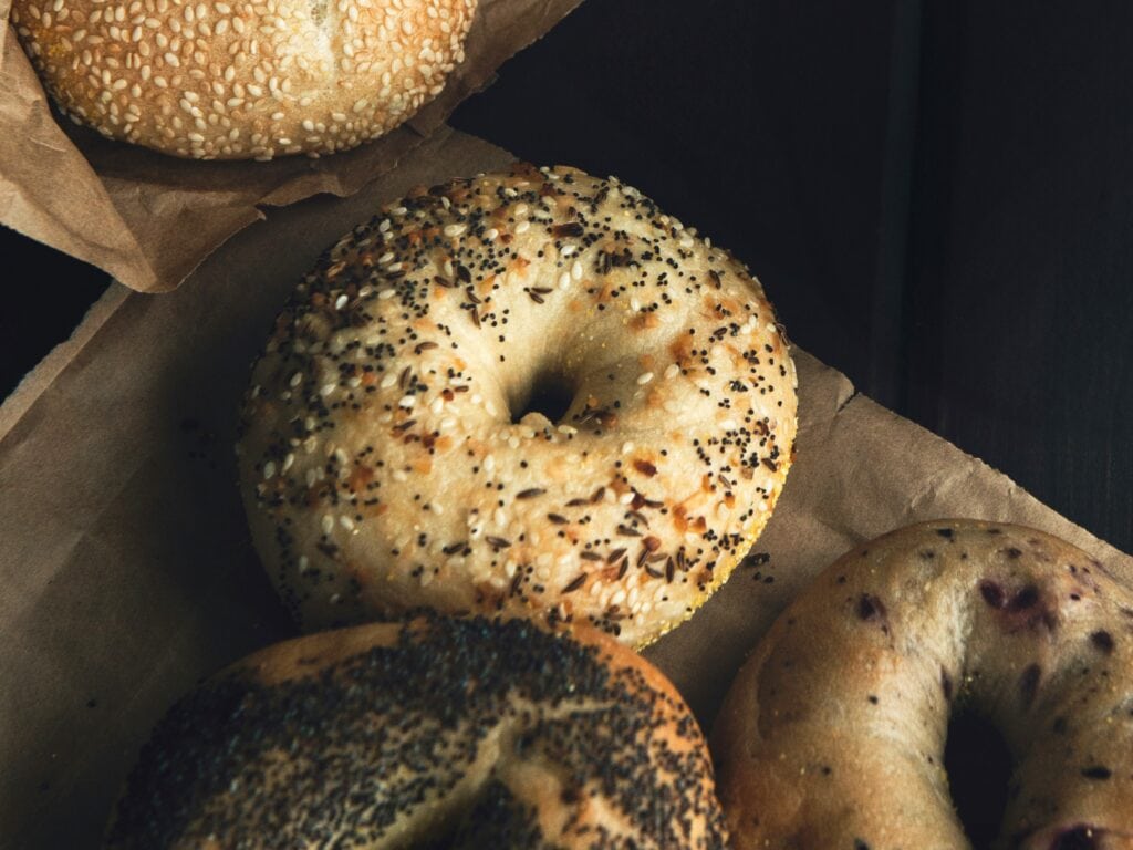 Assorted bagels with different toppings on brown paper, including sesame seeds, poppy seeds, and everything seasoning—New York insider tips for the best bagel experience.