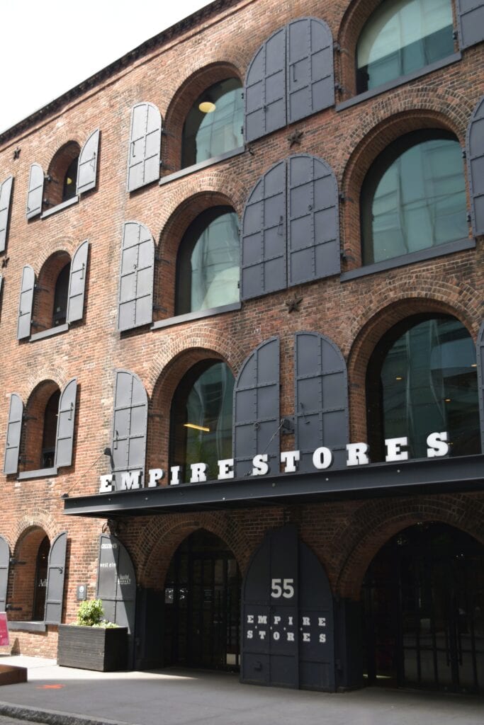 A brick building with arched windows and black shutters, labelled "Empire Stores" above the entrance, stands near the Brooklyn Bridge.