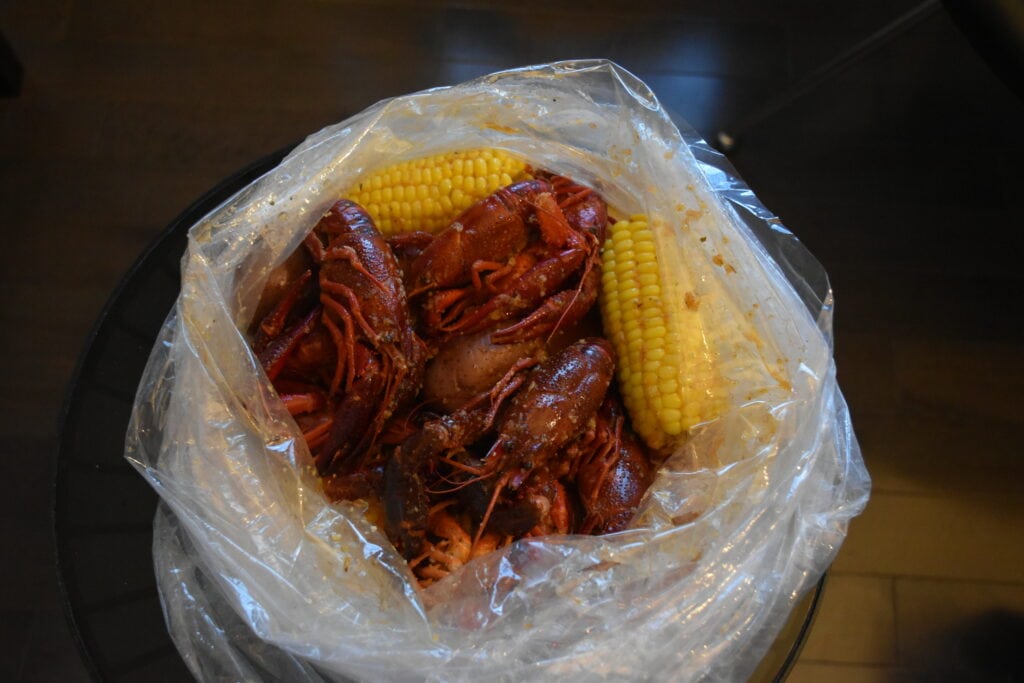 A plastic bag filled with cooked crayfish and corn on the cob sits on a dark table, serving up a taste of Southern comfort food in New York.