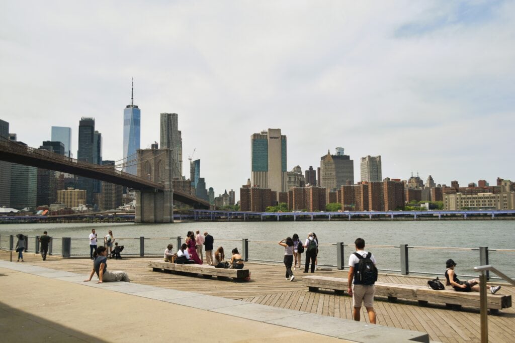 People unwind by the waterfront, taking in stunning views of the Brooklyn Bridge and the Manhattan skyline in the background.