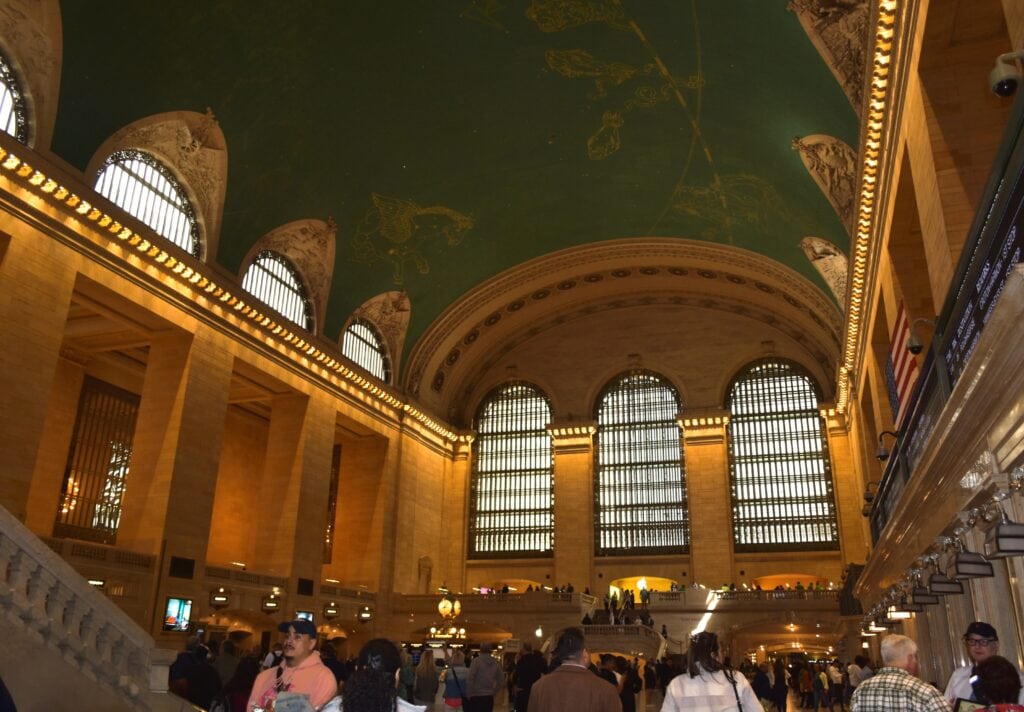 Grand Central Station’s main concourse buzzes with crowds beneath large arched windows and a striking green celestial ceiling.