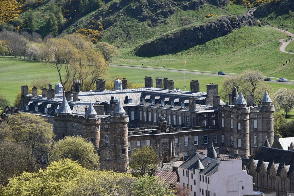 A large historic stone palace with turrets, set against green hills and open parkland, stands among the best attractions Edinburgh has to offer.