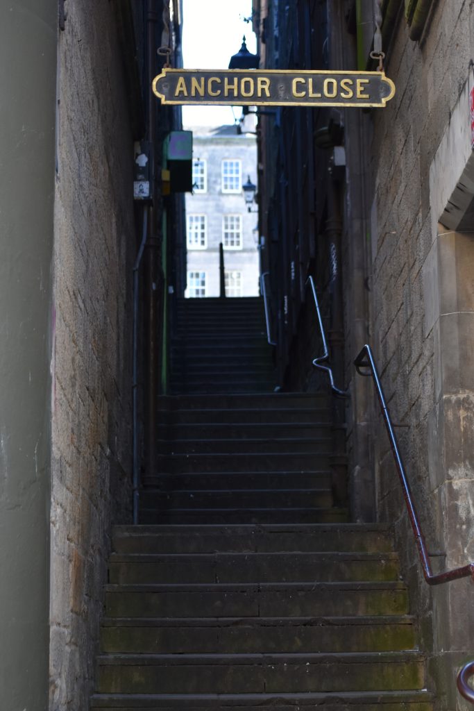 Narrow stone stairway between buildings, with a sign above reading "Anchor Close," leading to one of the best attractions Edinburgh has to offer.