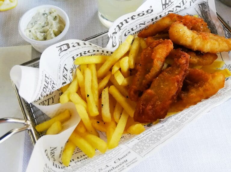 A tray of fish and chips on a table next to a newspaper.