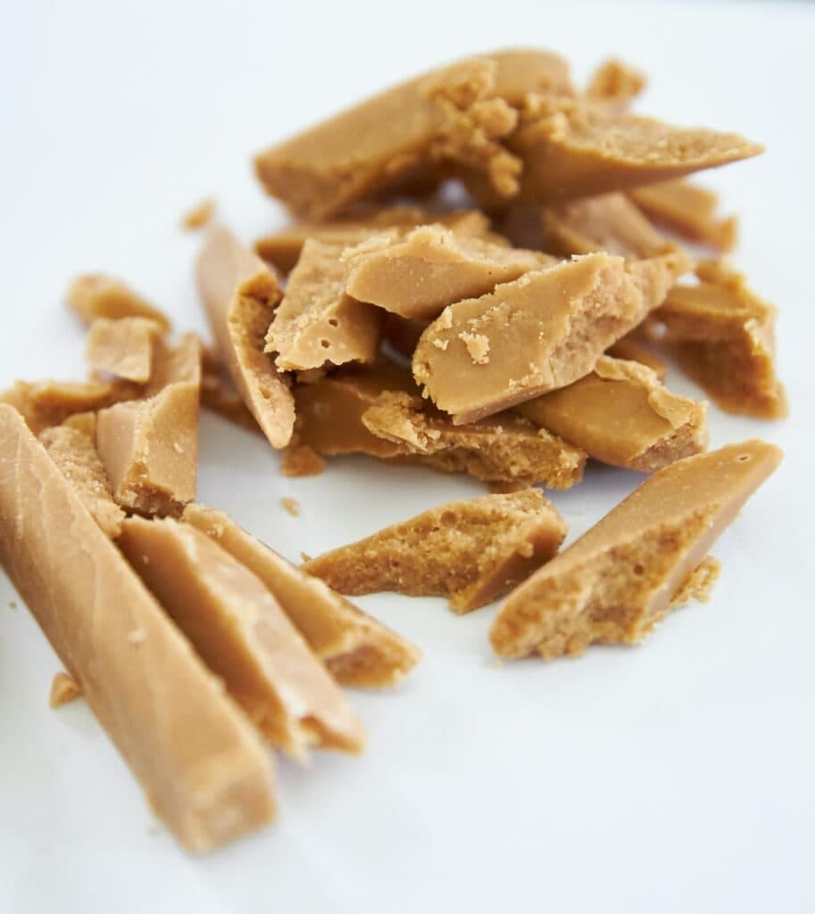 A pile of pieces of peanut brittle on a white plate.