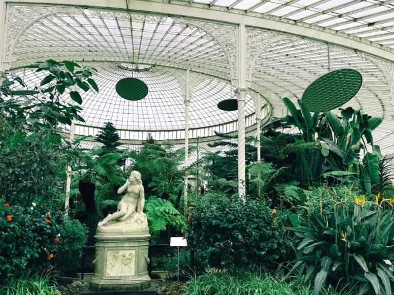 A greenhouse filled with a variety of plants and featuring a statue in the Glasgow Botanic Gardens.
