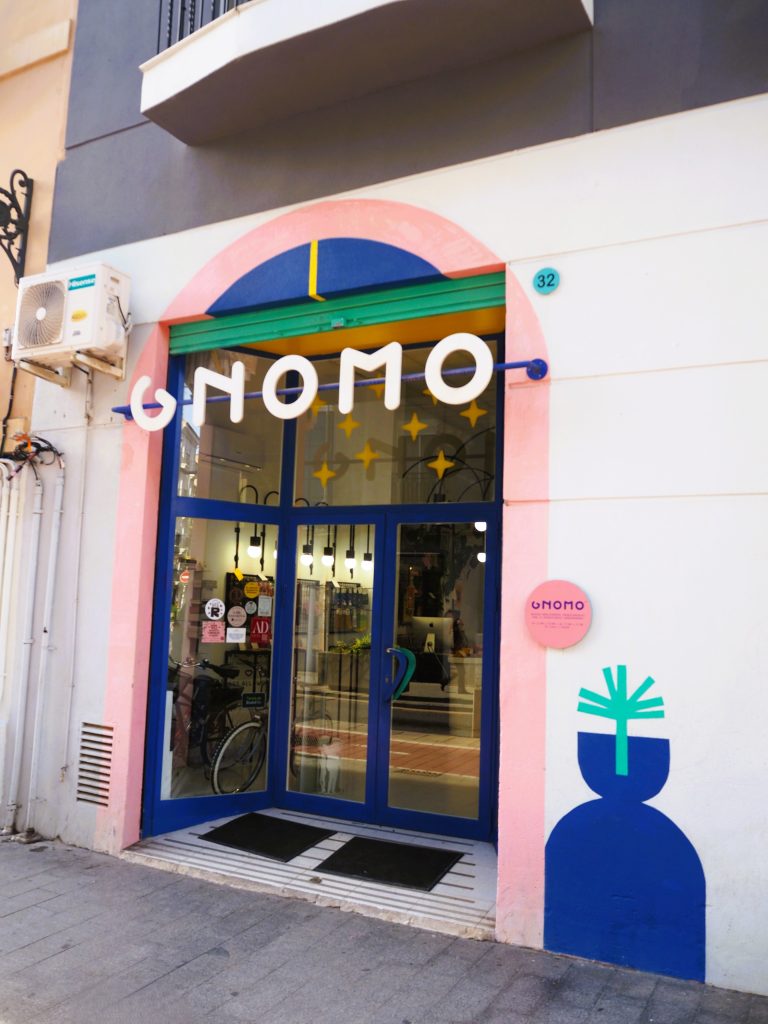 Colorful storefront with “ONOMO” sign, pink arch, blue door, and abstract blue vase art on the wall—capturing the vibrant spirit found in popular neighborhoods in Valencia.