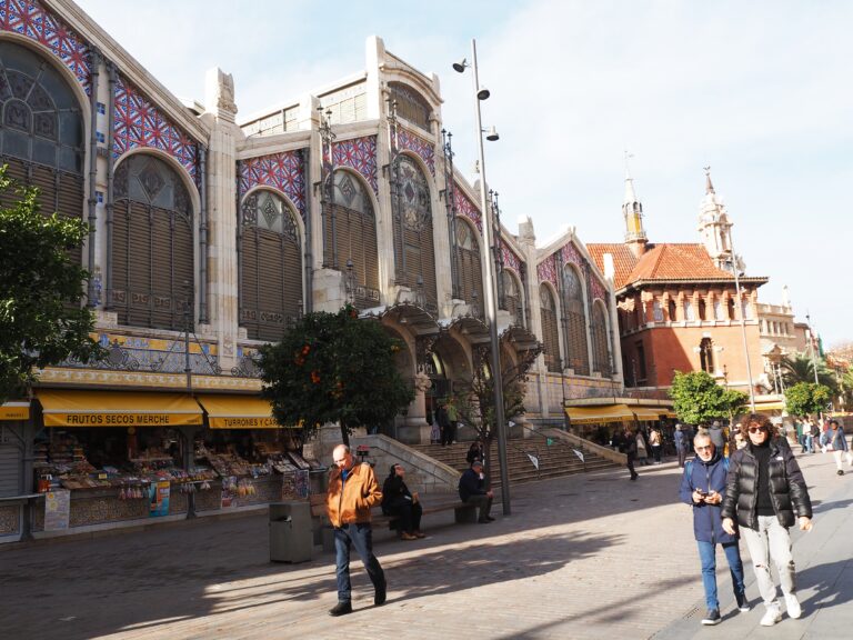 People walk outside a large, ornate market building with colourful tile details and street vendors—one of the highlights on any list of the 7x Best things to Do in Valencia.