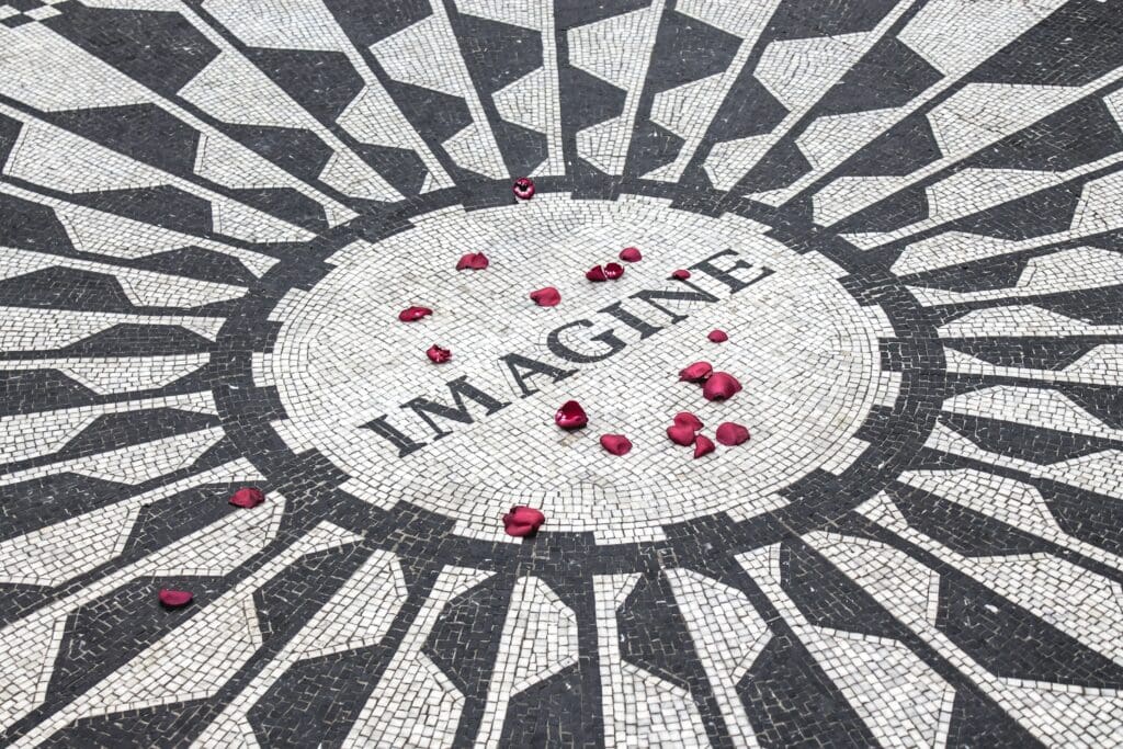A red rose is placed in the middle of a mosaic floor with the word imagine.