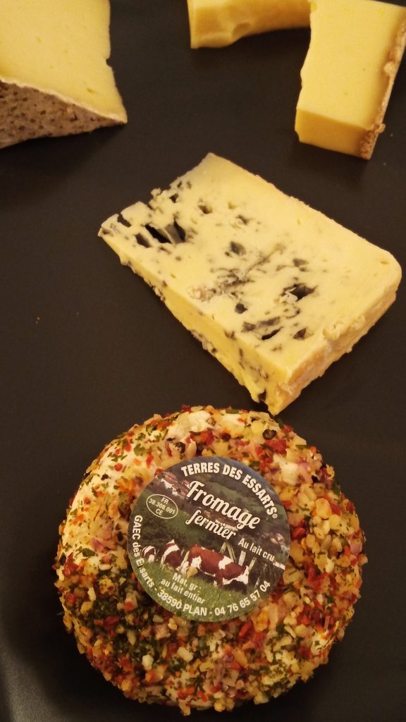 Four assorted cheese pieces on a dark plate, including a herb-coated round cheese in the foreground—a selection that belongs on any 5x Must try French Food list.
