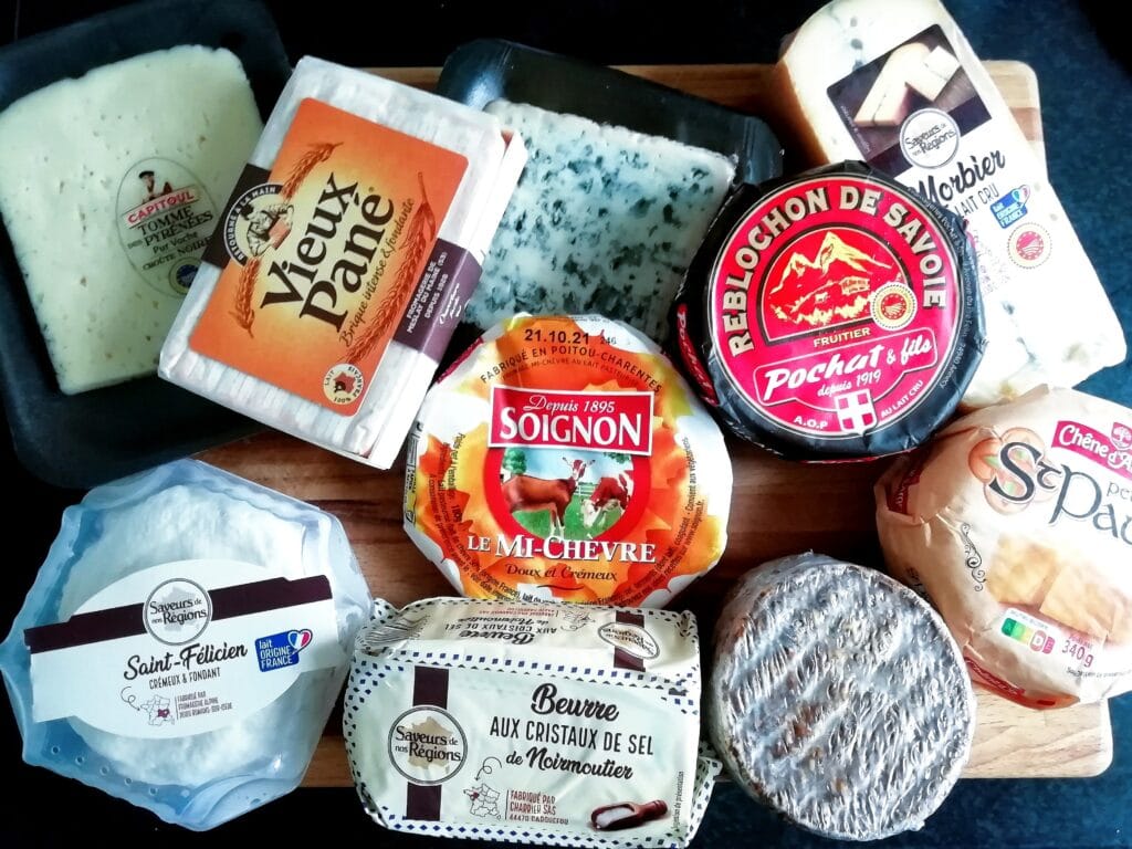 A selection of various French cheeses arranged on a wooden board, with colourful labels visible—a 5x must-try French food experience.