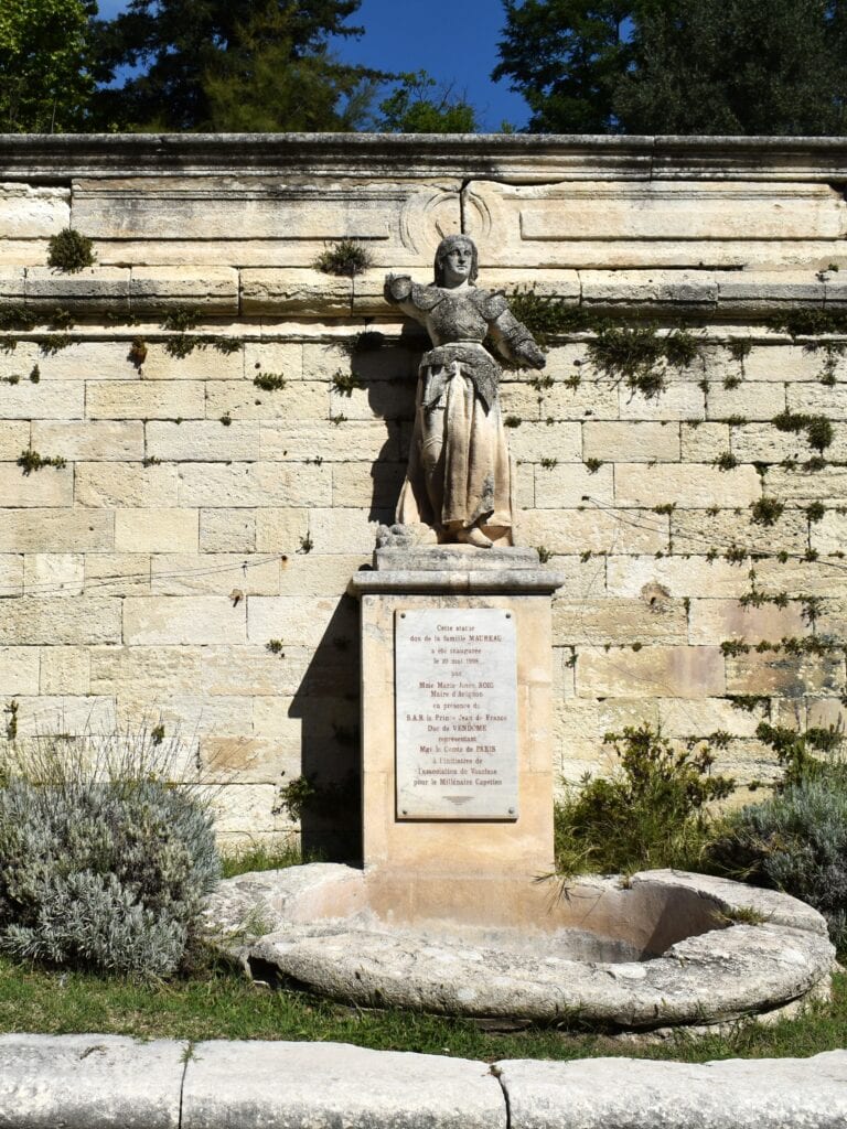 Stone statue of a medieval knight above a fountain and plaque, set against an old stone wall with some greenery—one of the 5x Best things to Do in Avignon for history lovers.