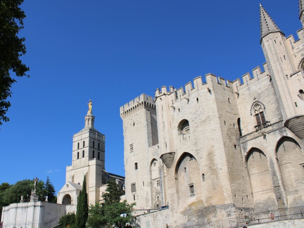 Stone fortress and church with golden statue under a clear blue sky, viewed from below—one of the 5x Best things to Do in Avignon.