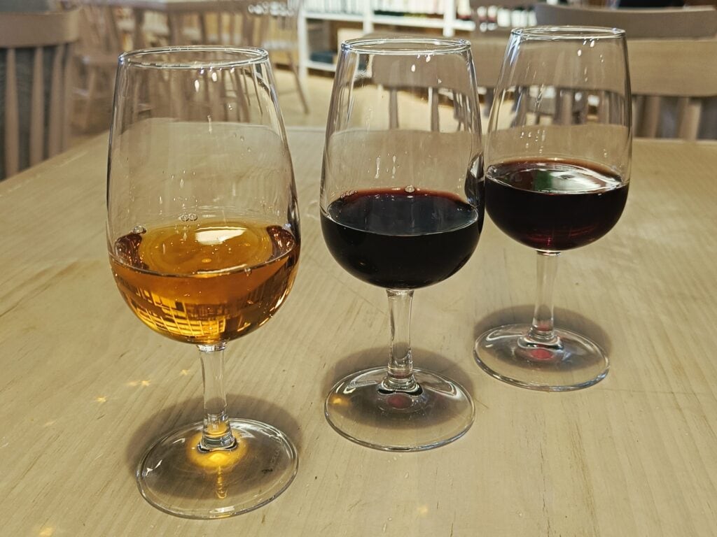 Three glasses of wine—one white, one red, and one rosé—on a wooden table in a restaurant setting, reminiscent of the best wine tastings near Avignon.