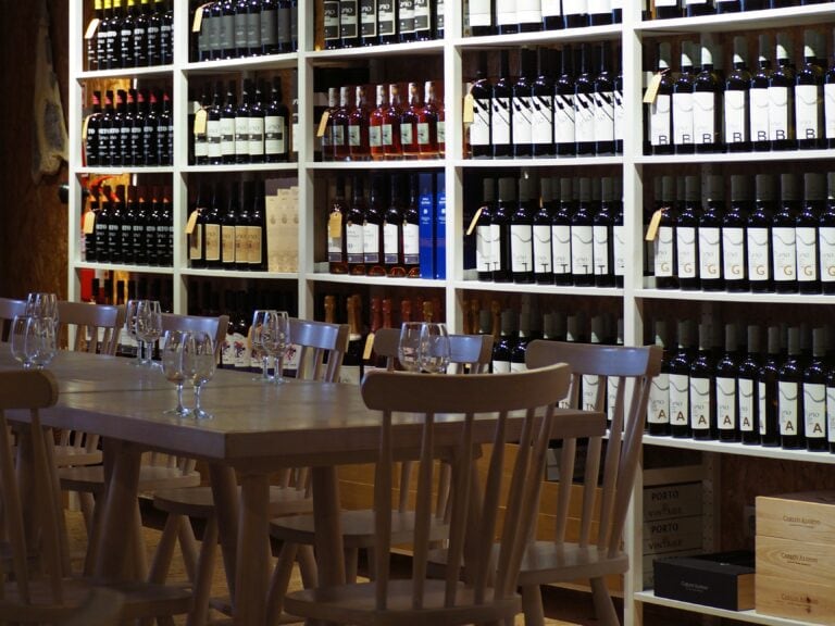 Wooden table and chairs in front of shelves filled with wine bottles create a cosy vibe in this wine shop—a must do: wine tastings near Avignon for any enthusiast.