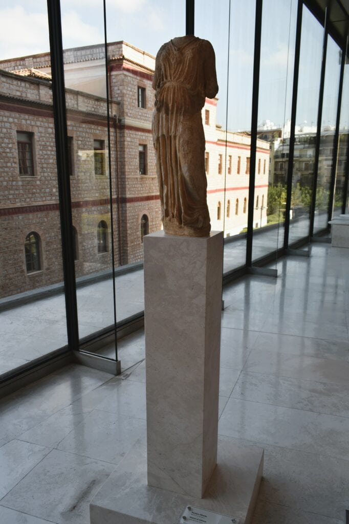 A statue on a pedestal in front of a building. athens nct