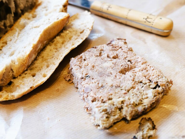 A loaf of bread with meat on it and a knife.