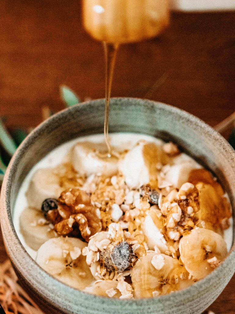 A bowl of granola with bananas and walnuts being drizzled with Greek honey.