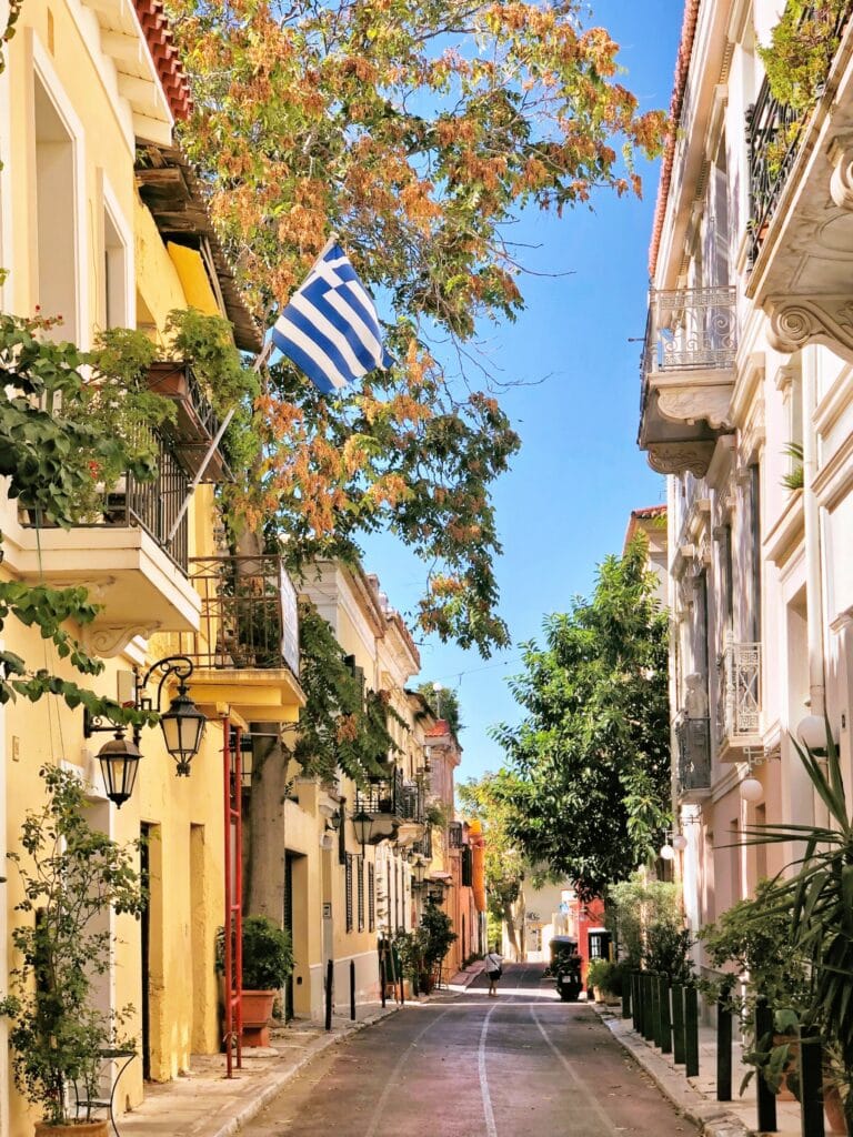 A narrow street in greece with a greek flag flying.