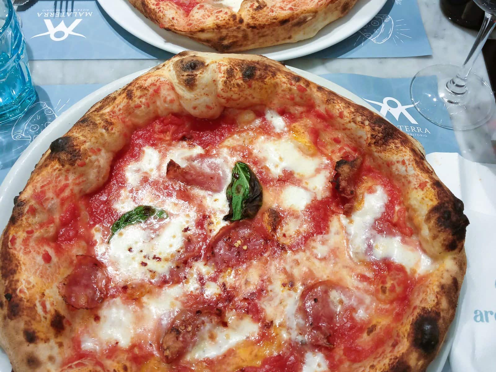 An Italian pizza on a plate next to a glass of wine.