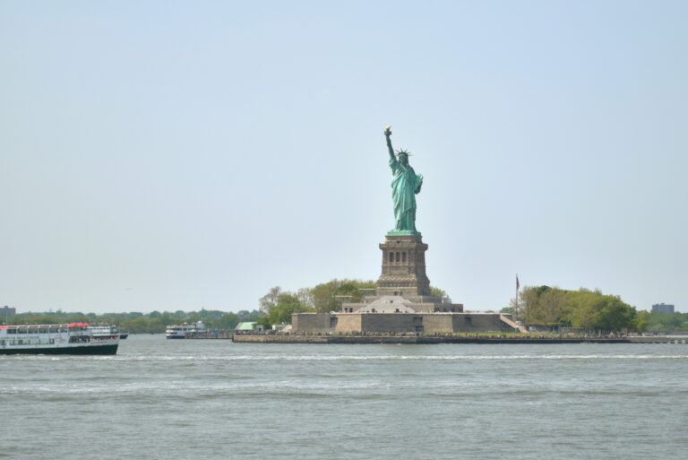 The iconic Statue of Liberty stands tall on Liberty Island as a ferry gracefully approaches through the shimmering waters.