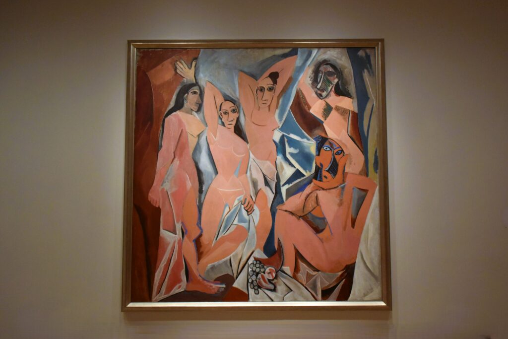 A painting of five abstract nude figures in warm tones, framed and displayed on a museum wall—just one of many striking works you can see when you visit MoMA in New York (Museum of Modern Art).