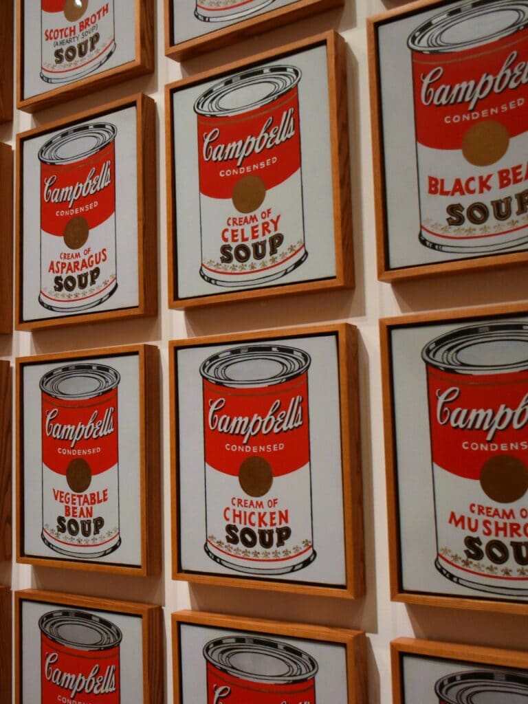 Framed Campbell’s soup tin artworks, each showing a different flavour, displayed in a grid pattern on a wall—see this iconic pop art when you visit MoMA in New York (Museum of Modern Art).