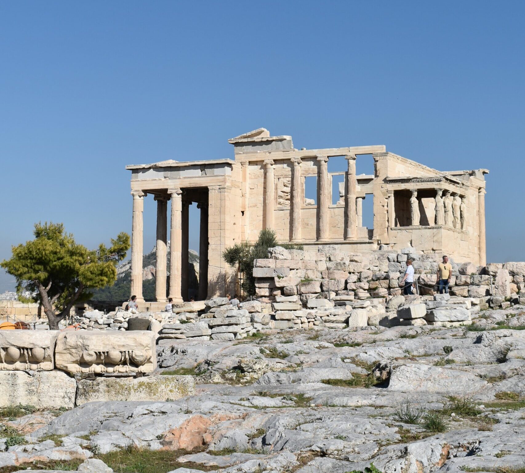 Ancient Greek ruins of the Erechtheion temple on the Acropolis of Athens, with clear blue skies in the background.