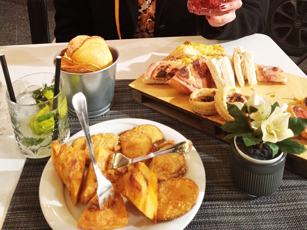 It's aperitivo time in Rome: a table adorned with assorted appetizers, chips, and drinks; a person gracefully holding a glass.