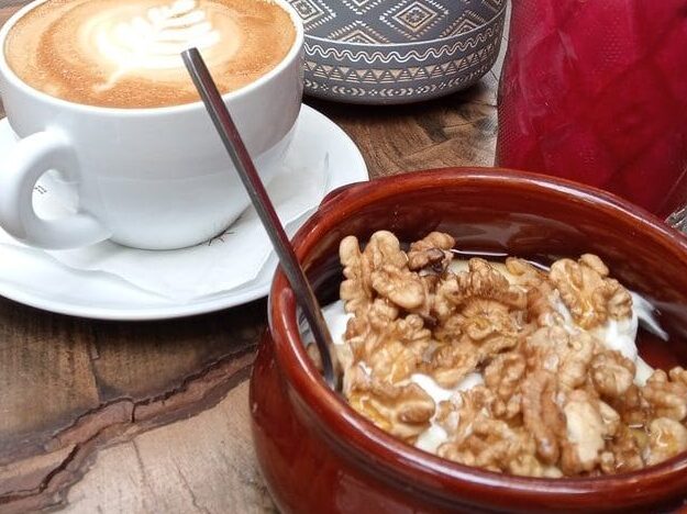 A wooden table with a cup of coffee and a bowl of cereal.