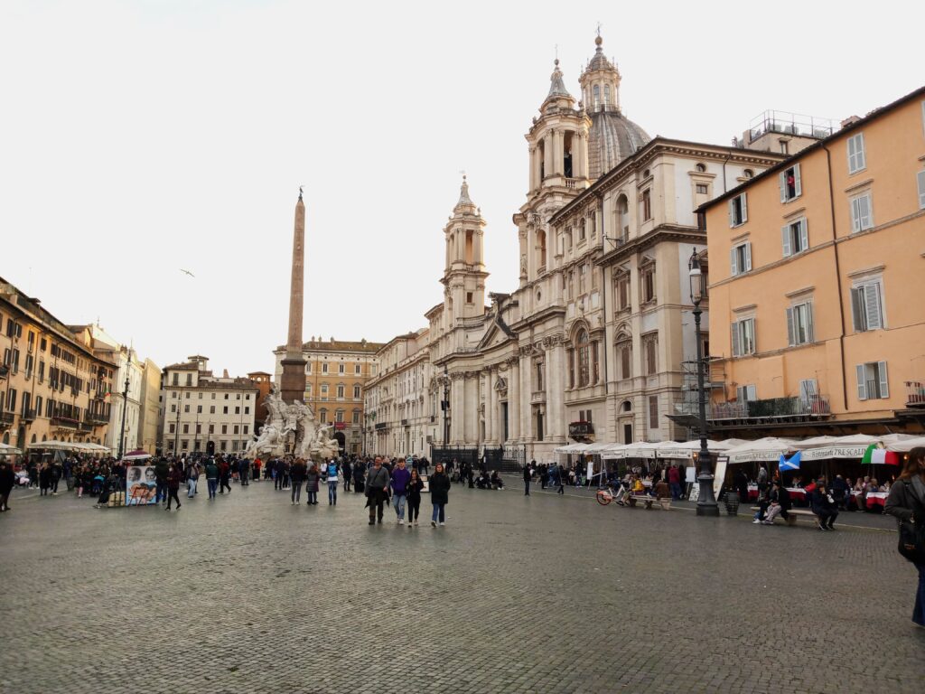 Piazza Navona, one of the must-see attractions in Rome, buzzes with crowds admiring its historic buildings and towering obelisk under a clear sky.