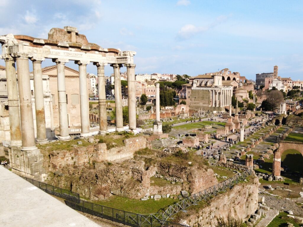 A sunny view of the Roman Forum, one of the must-see attractions in Rome, with ancient ruins and columns under a blue sky.