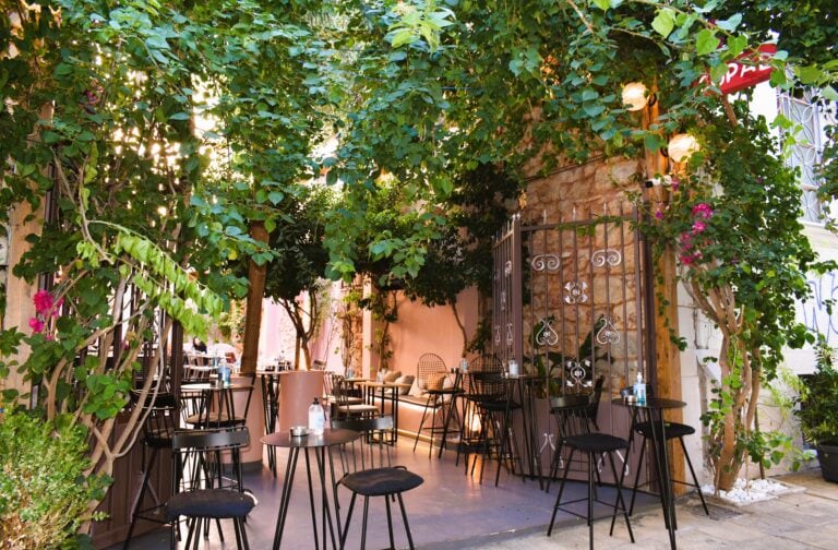 Outdoor café in Athens with tables and chairs shaded by lush greenery, creating a cozy and inviting atmosphere. Often listed among the city's best restaurants.