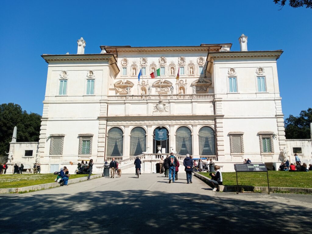 Front view of Villa Borghese, one of the must-see attractions in Rome, with visitors outside enjoying a sunny day.