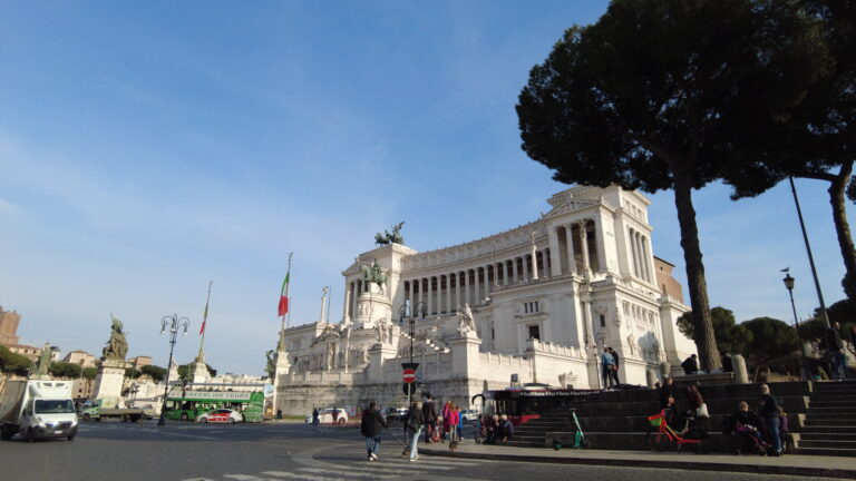 The impressive large white monument in Rome stands proudly with the Italian flag waving, as people sit nearby taking in one of the best things to do in Rome.