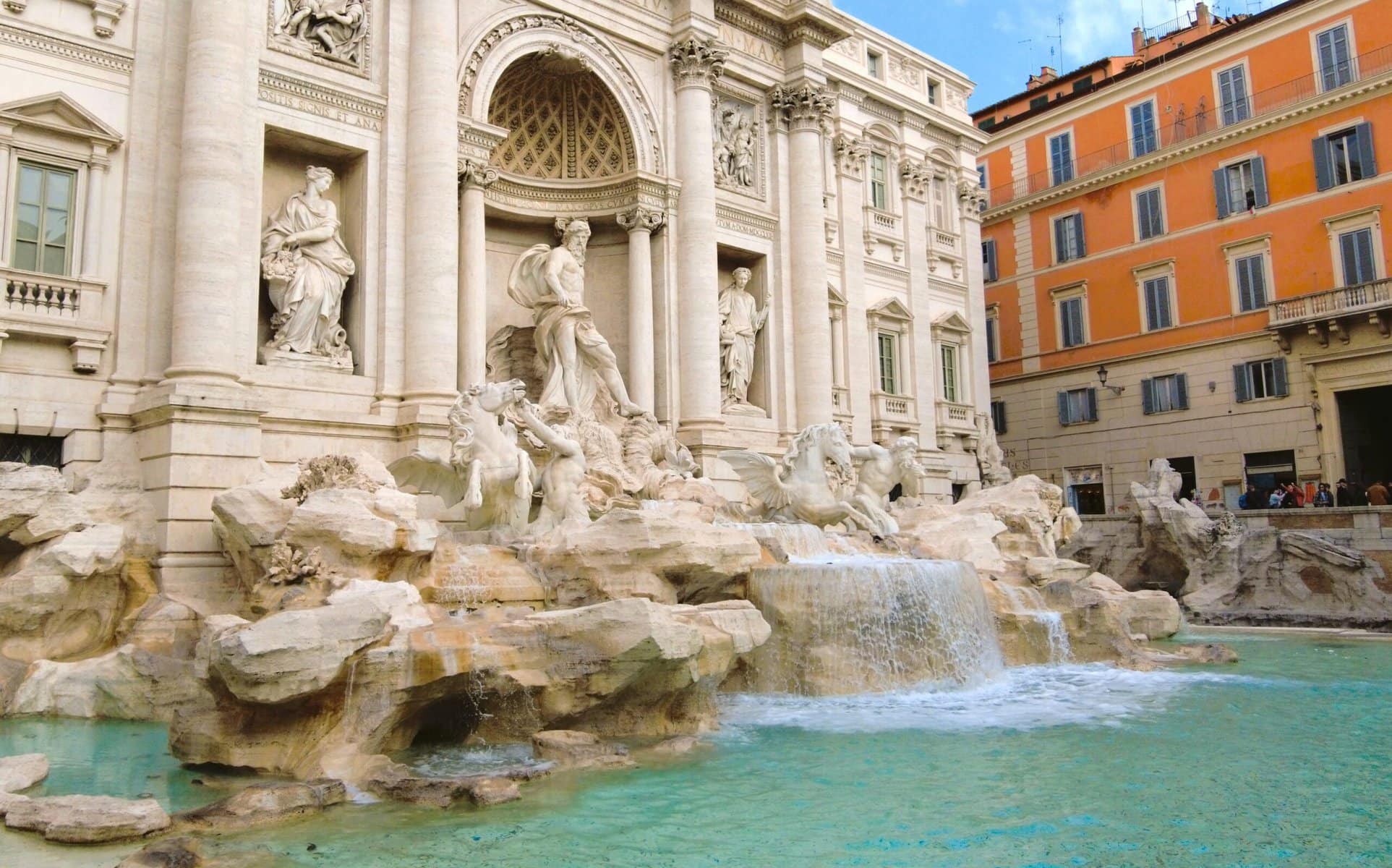 The Trevi Fountain, one of the must-see attractions in Rome, boasts ornate sculptures and flowing water under a bright blue sky.
