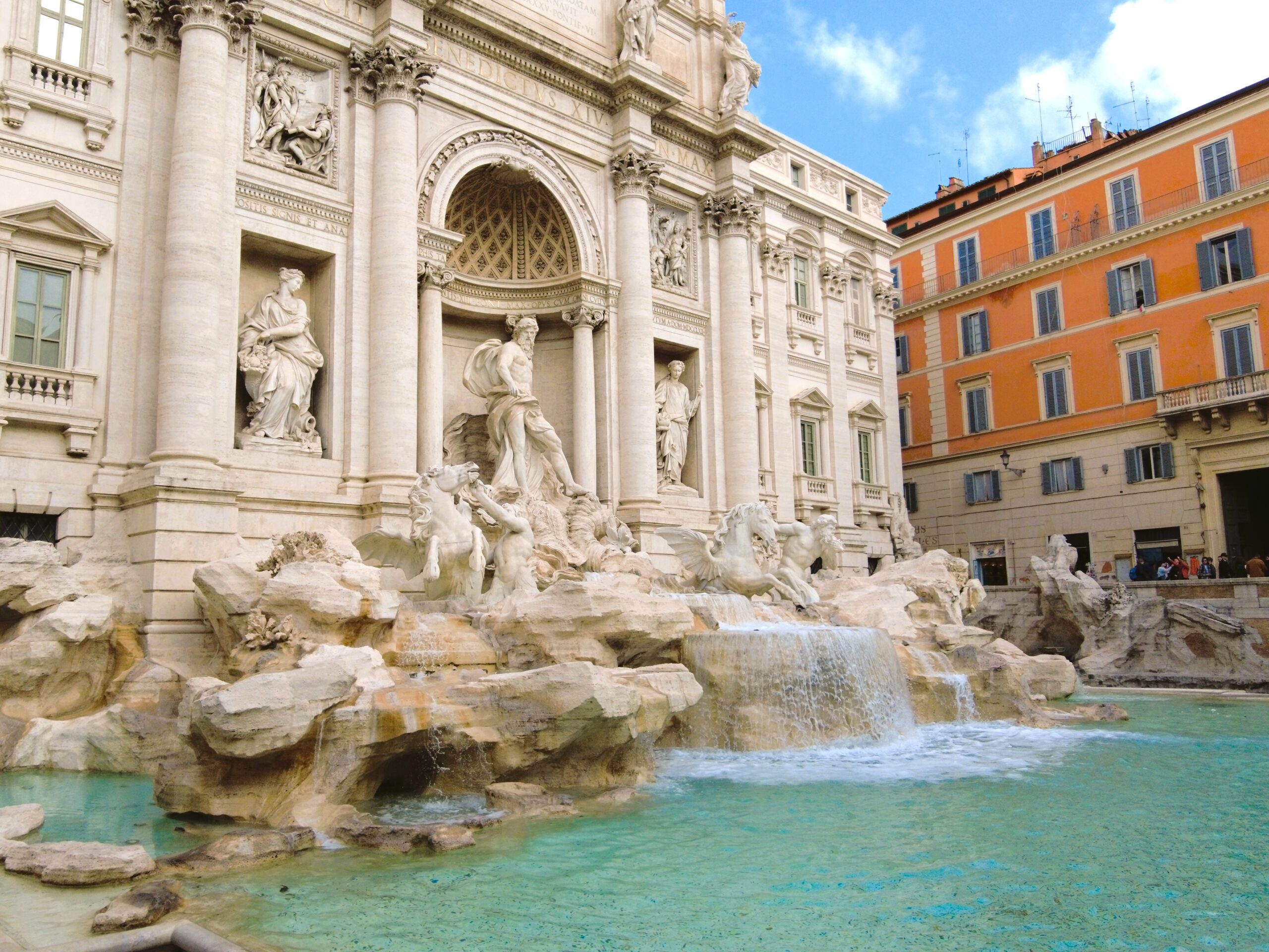 The Trevi Fountain, one of the must-see attractions in Rome, boasts ornate sculptures and flowing water under a bright blue sky.