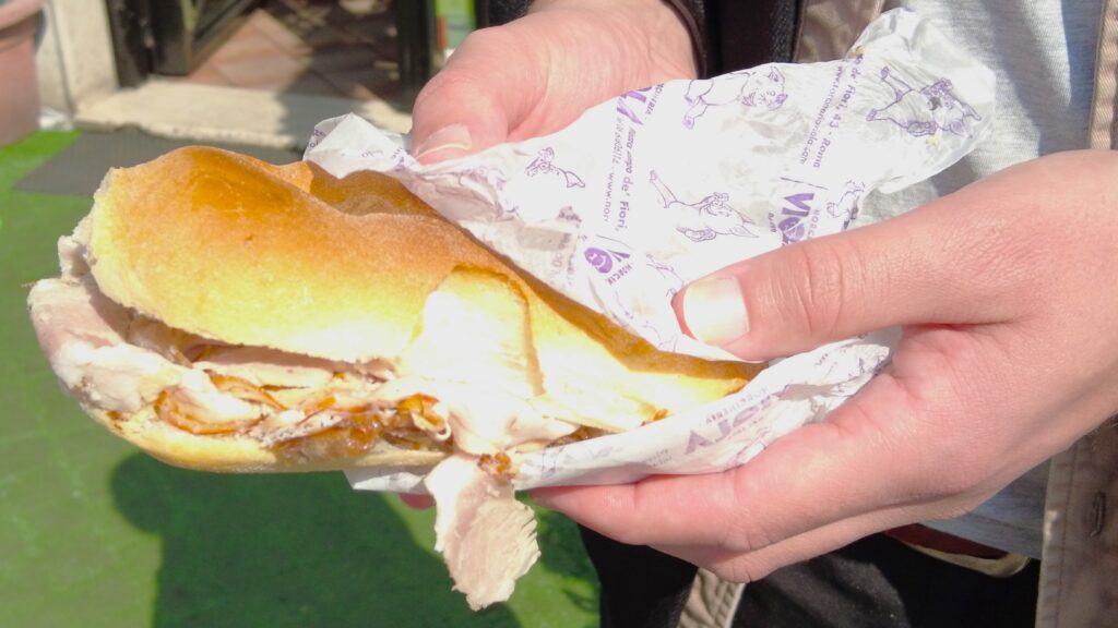 A person eagerly holds a sandwich with sliced meat, wrapped in white paper—a simple yet delicious representation of The Best Italian Food.