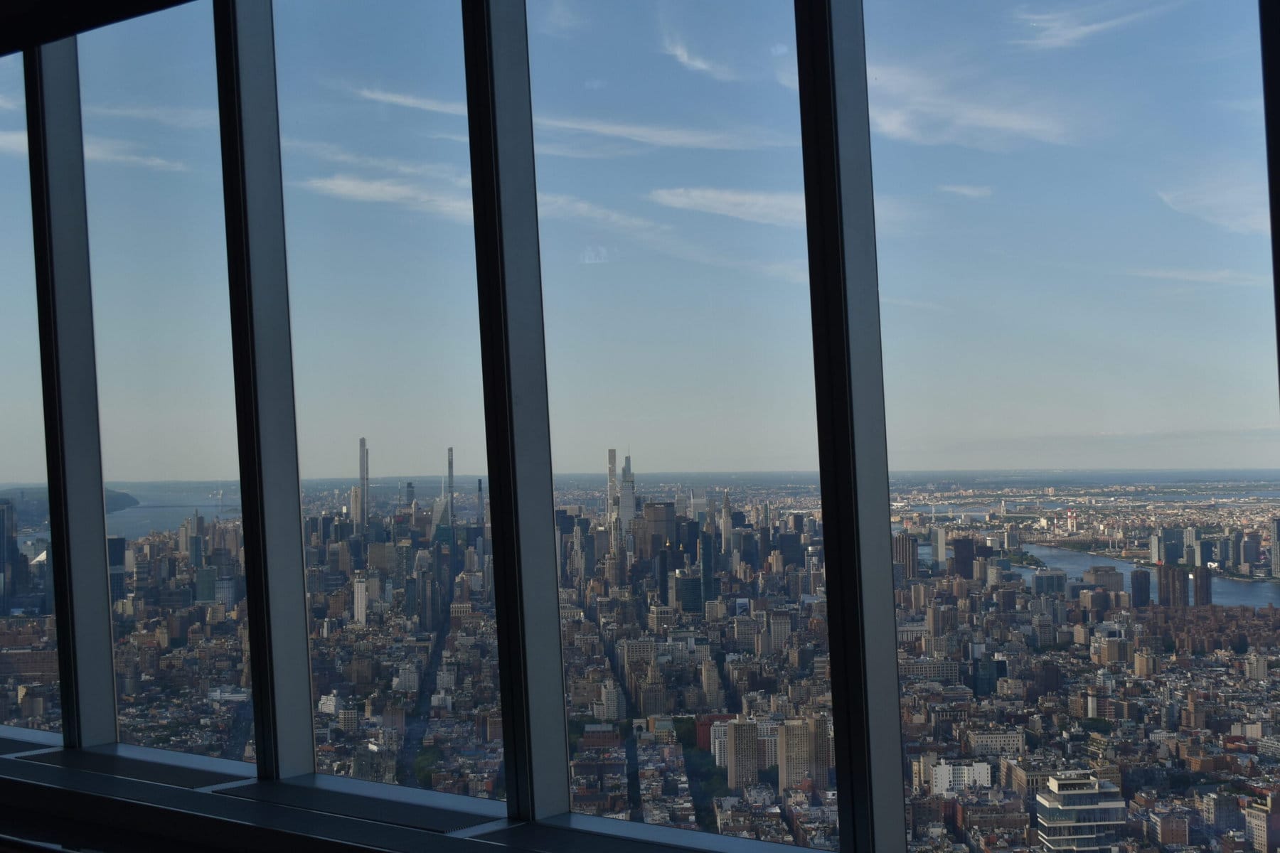 View of New York City skyline from an indoor observation deck with large glass windows on a clear day.