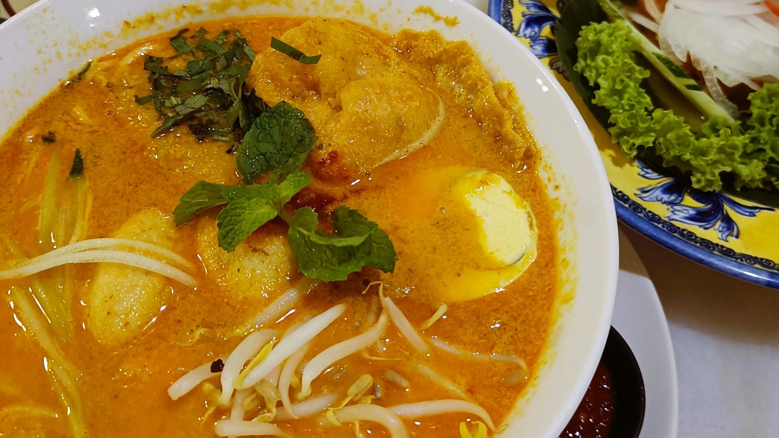 A table with must-try food in Singapore: laksa noodle soup, beef rendang, and nasi lemak, each dish garnished with fresh herbs and vibrant vegetables.