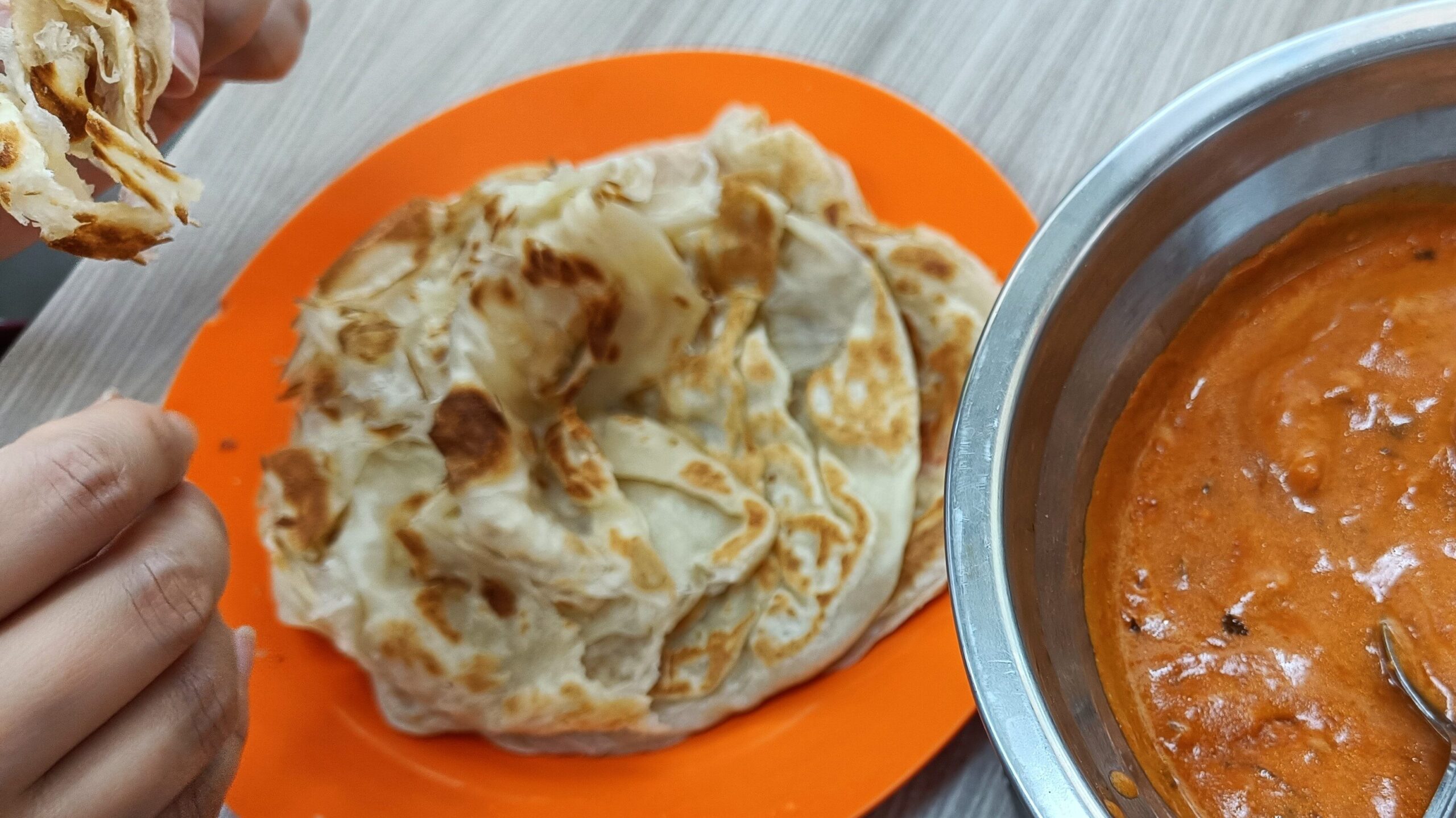 A person savors tearing flatbread beside a bowl of curry on a table, an iconic must-try experience for any food lover exploring the vibrant flavors of Singapore.