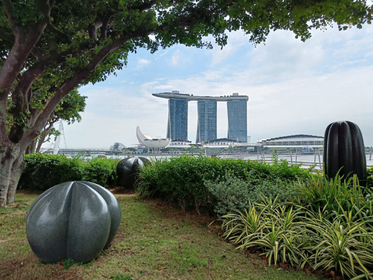 Garden view with sculpture and trees, overlooking a modern, three-tower building in the background—one of the most popular attractions in Singapore.