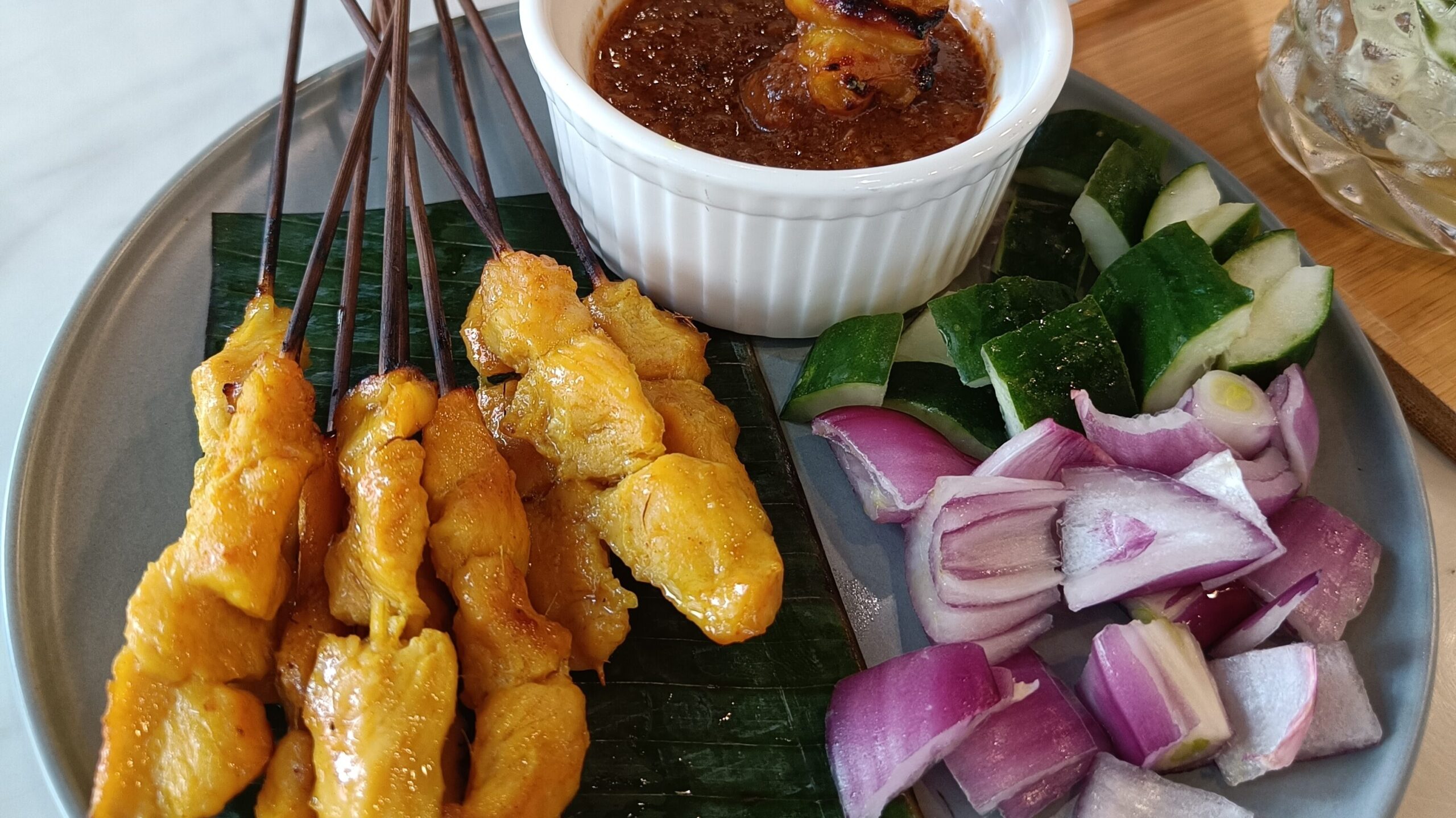 Chicken satay skewers with peanut sauce, sliced red onions, and cucumbers on a plate - a must-try food experience in Singapore.