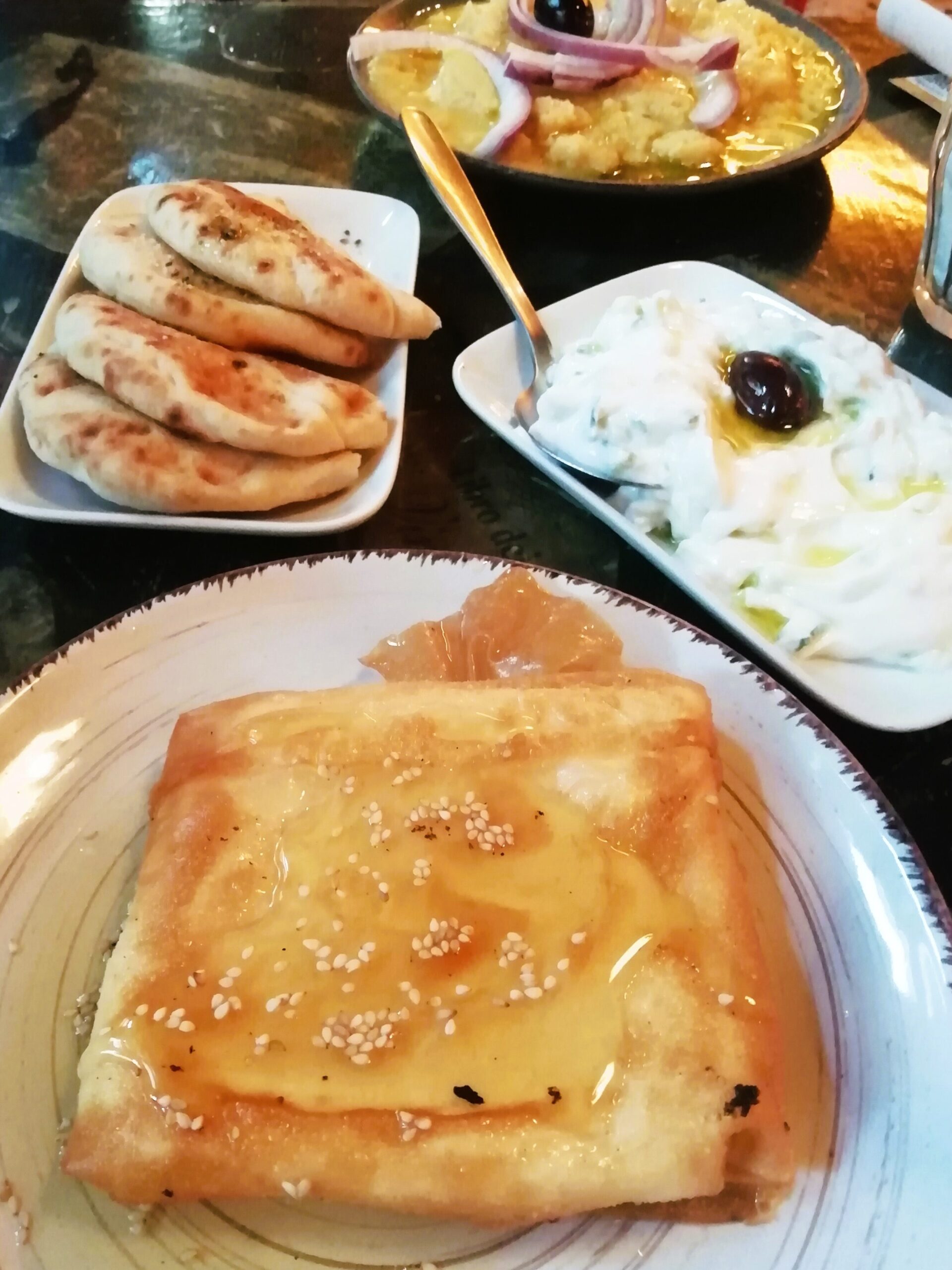 At one of Athens' best restaurants, enjoy a Greek food spread featuring pita bread, savory dip, honey-covered pastry, and a delightful plate of what appears to be fava.