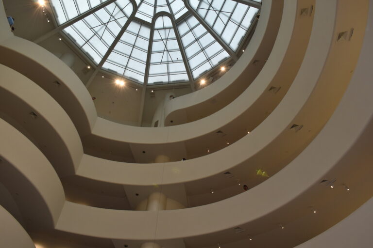 Interior view of the Guggenheim New York, featuring a spacious spiraling ramp beneath a breathtaking glass dome ceiling.