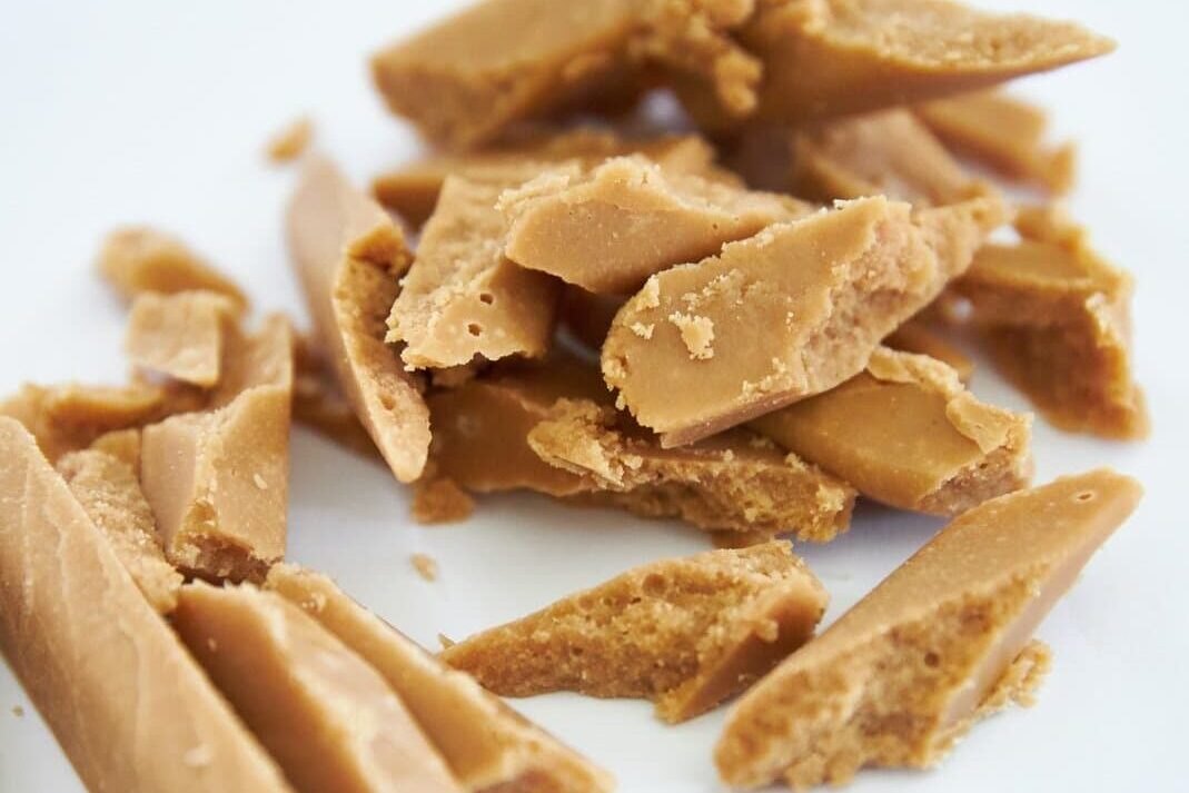 A pile of pieces of peanut brittle on a white plate.