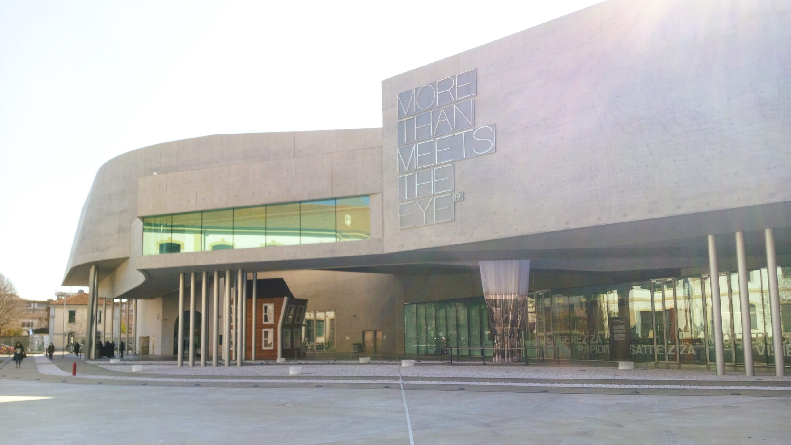 In a popular Rome neighborhood, a modern building with large windows and curved architecture stands proudly. A sign declares, "More Than Meets the Eye.